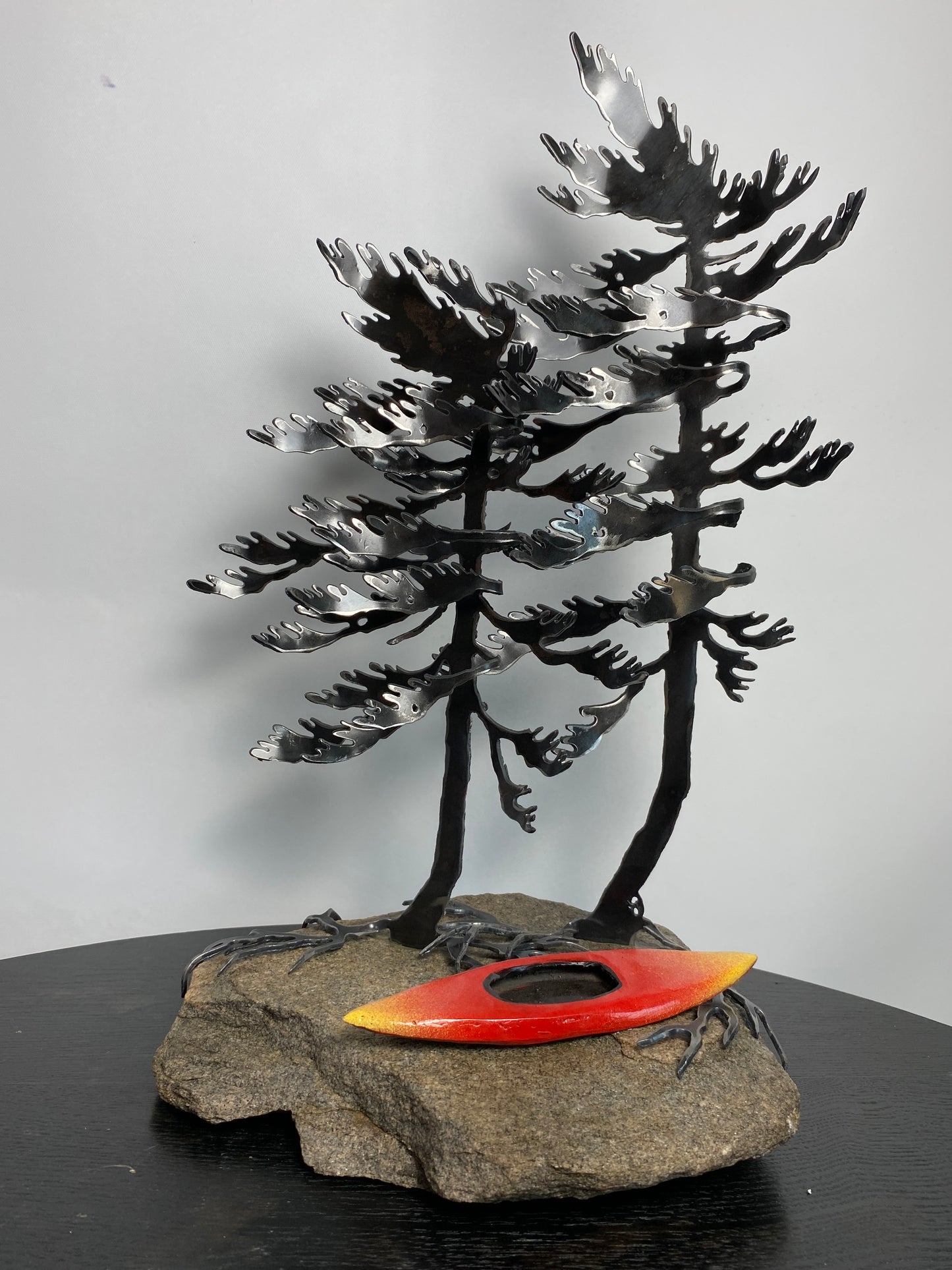 Metal windswept tree with kayak on granite