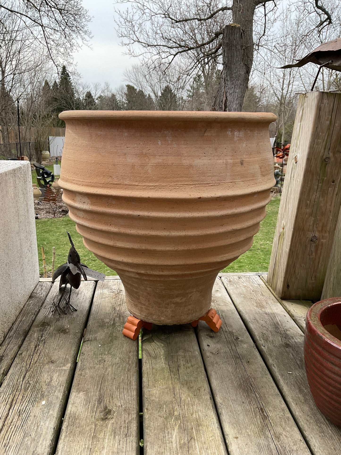 Large terracotta pot on a wooden deck with trees and grass in the background