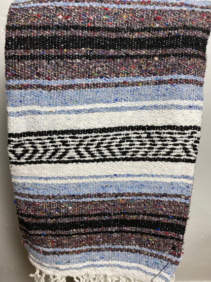 A woven textile blanket or throw with horizontal stripes in black, white, light blue, brown, and multicolored flecks, finished with a fringed edge. Falsa blanket from Mexico