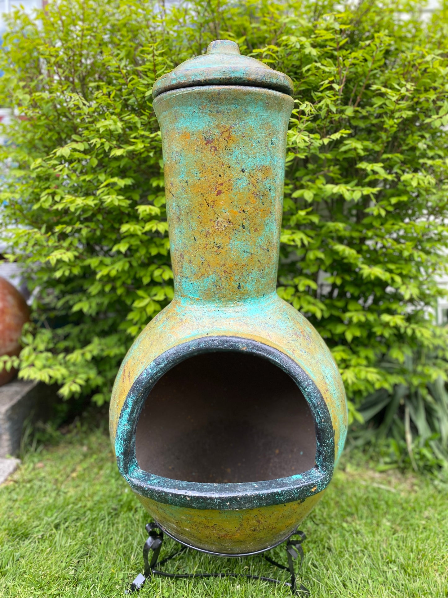 Decorative outdoor chiminea with a greenish-blue patina in a garden setting.