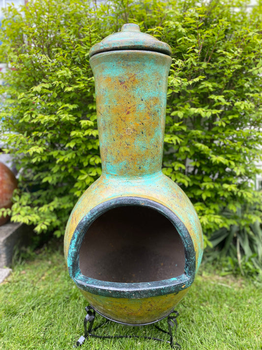 Decorative outdoor chiminea with a greenish-blue patina in a garden setting.