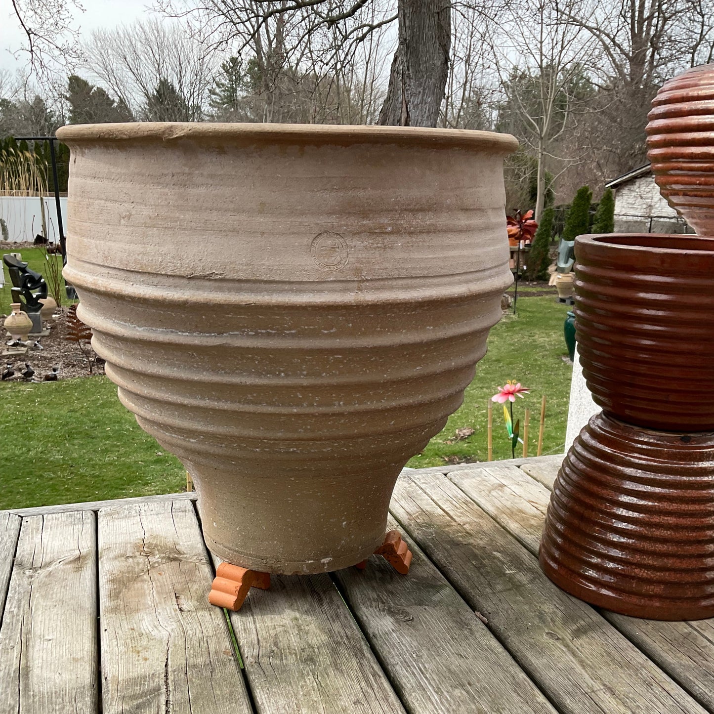 Large beige pot on a wooden deck with a grassy area and trees in the background