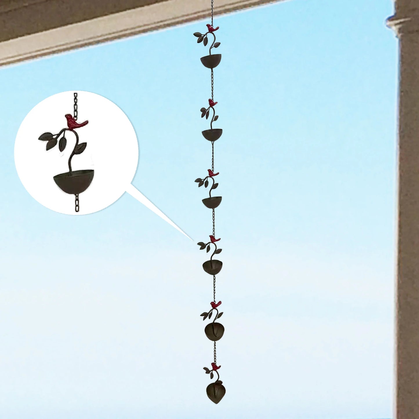 Decorative rain chain with bird and leaf design against a clear blue sky.