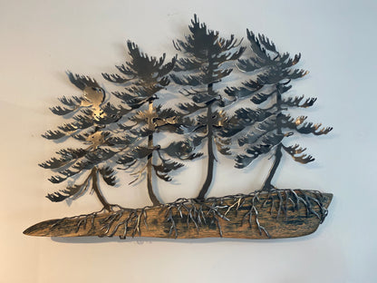 Metal wall art depicting three pine trees with exposed roots growing from a weathered log base, shown mounted against a plain light wall.