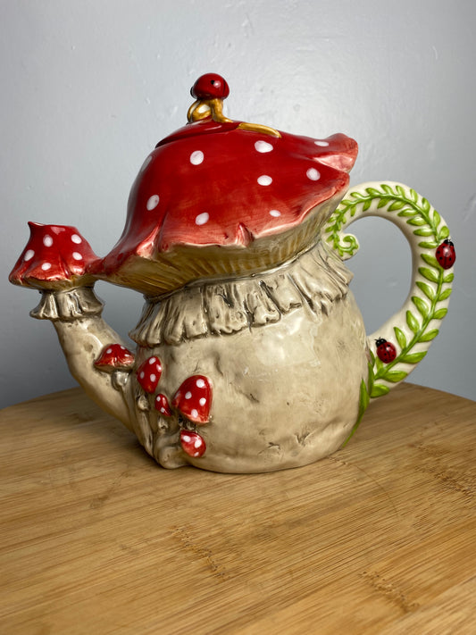 Decorative teapot with red polka dot mushroom design on a wooden look surface