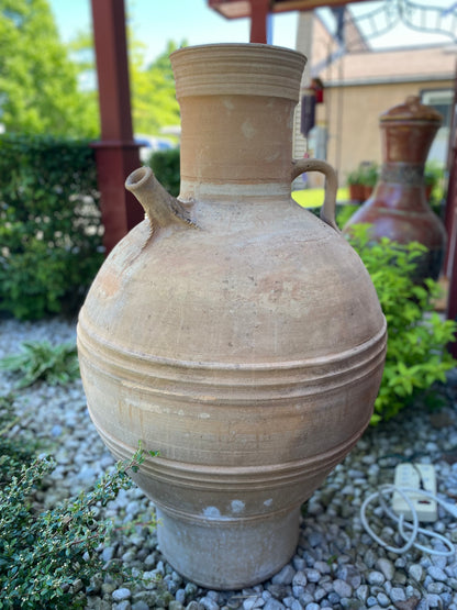 Large terracotta vase with handles on a gravel surface with greenery in the background